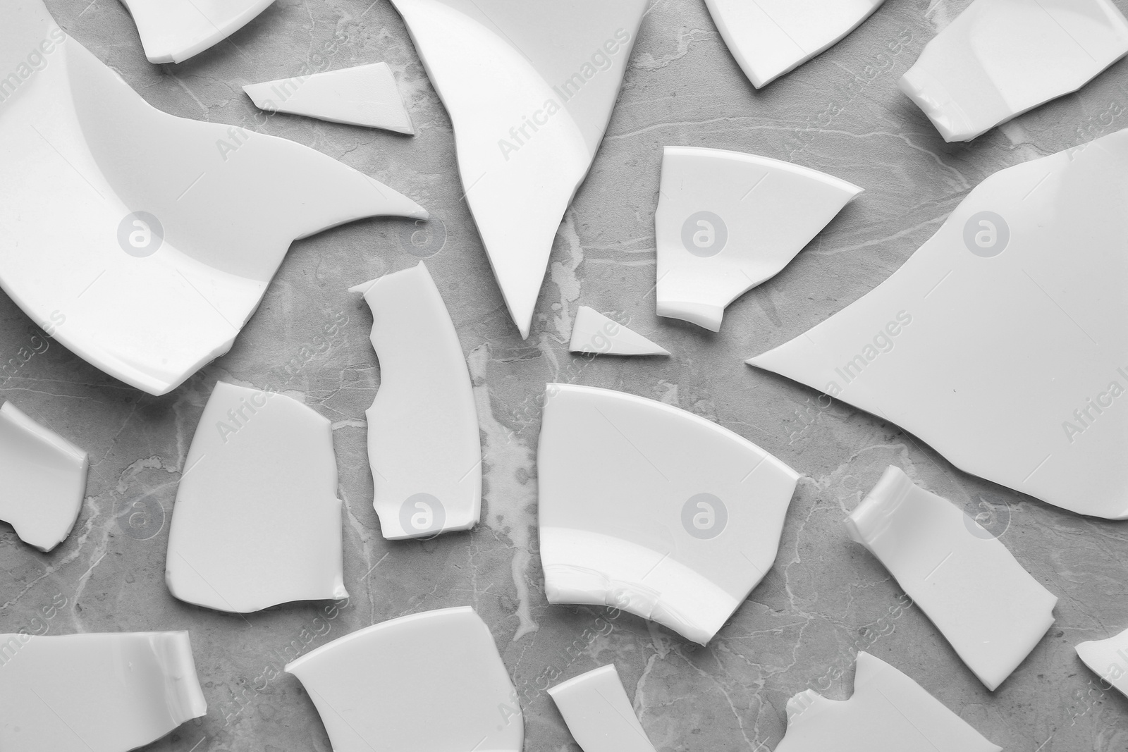 Photo of Pieces of broken ceramic plate on light grey table, flat lay