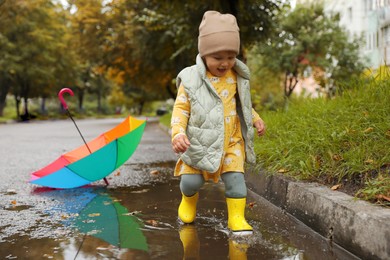 Cute little girl splashing water with her boots in puddle outdoors, space for text