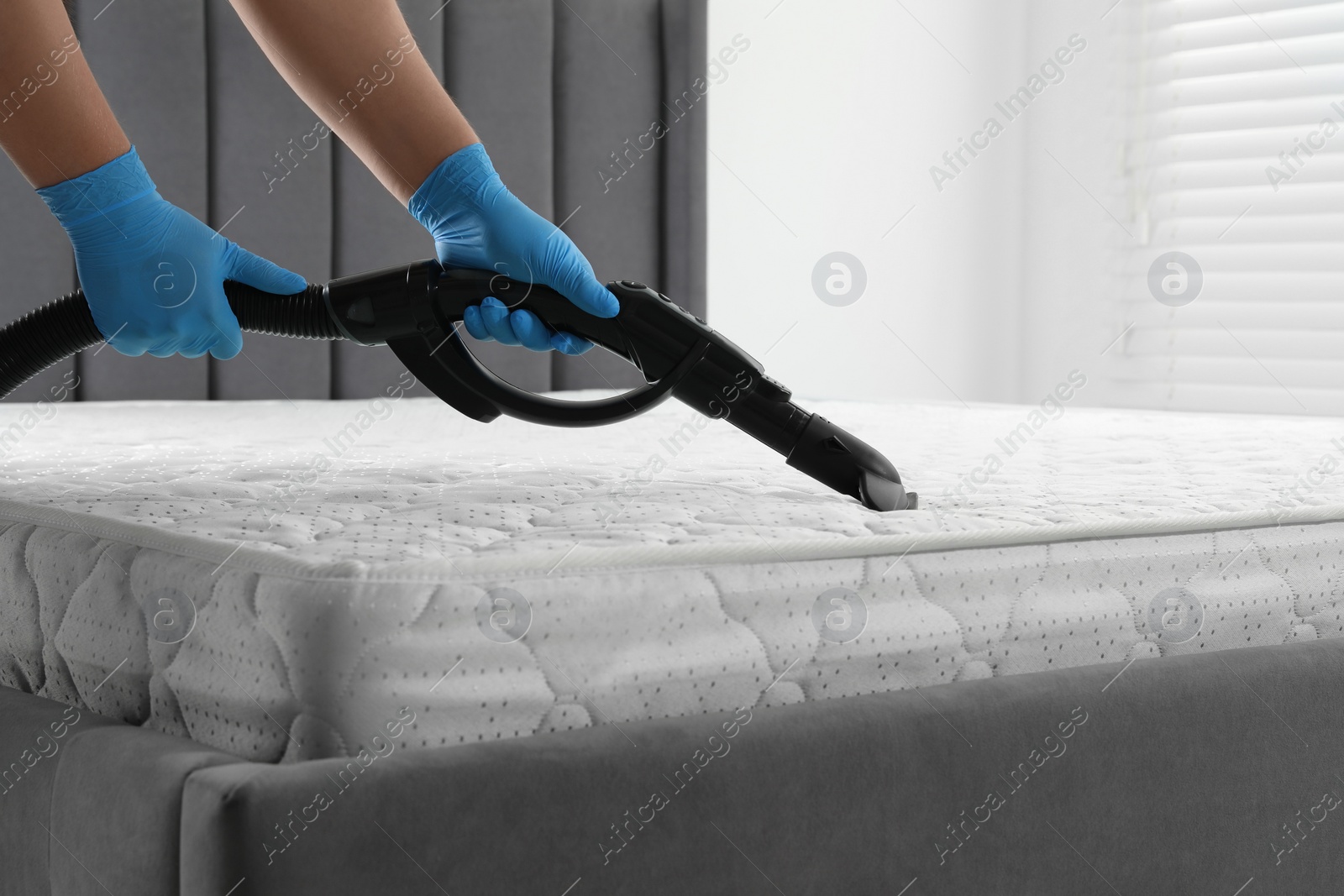 Photo of Woman disinfecting mattress with vacuum cleaner indoors, closeup