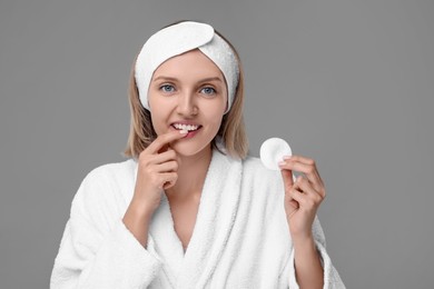 Young woman with cotton pad on light grey background