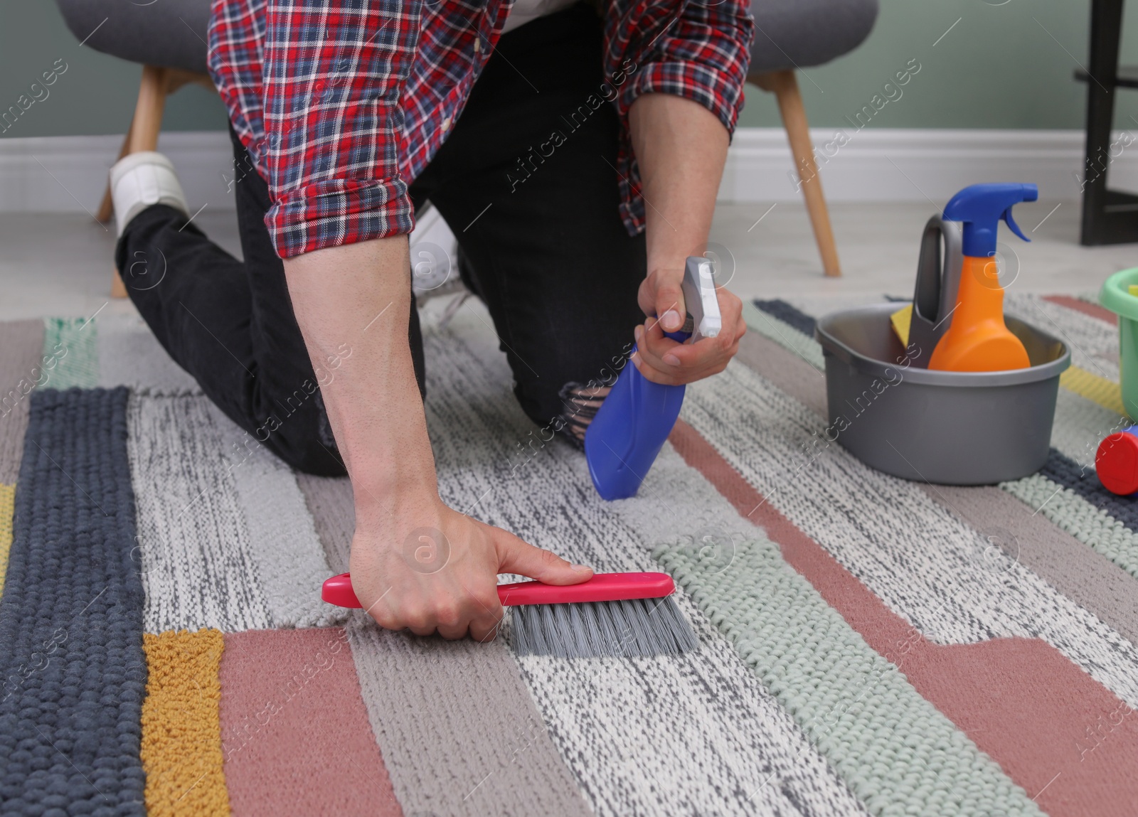 Photo of Young man cleaning carpet with brush at home