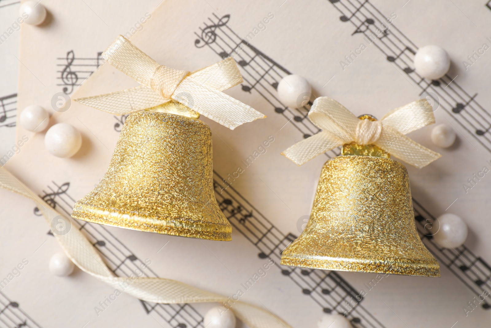 Photo of Golden shiny bells with white bows on music sheets, flat lay. Christmas decoration