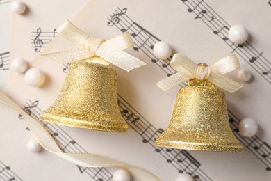 Photo of Golden shiny bells with white bows on music sheets, flat lay. Christmas decoration