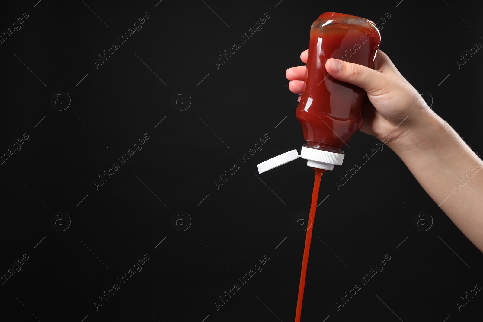 Photo of Woman pouring tasty ketchup from bottle on black background, closeup. Space for text