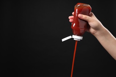 Photo of Woman pouring tasty ketchup from bottle on black background, closeup. Space for text