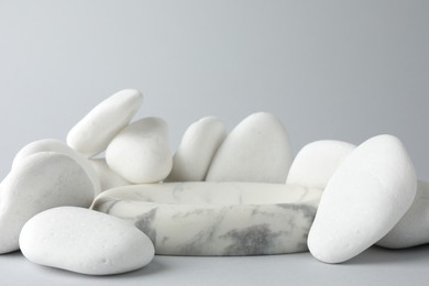 Photo of Presentation for product. Stone podium and pebbles on light grey background. Space for text