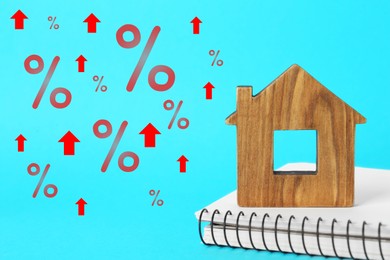 Mortgage rate rising illustrated by upward arrows and percent signs. House model and notebook on light blue background