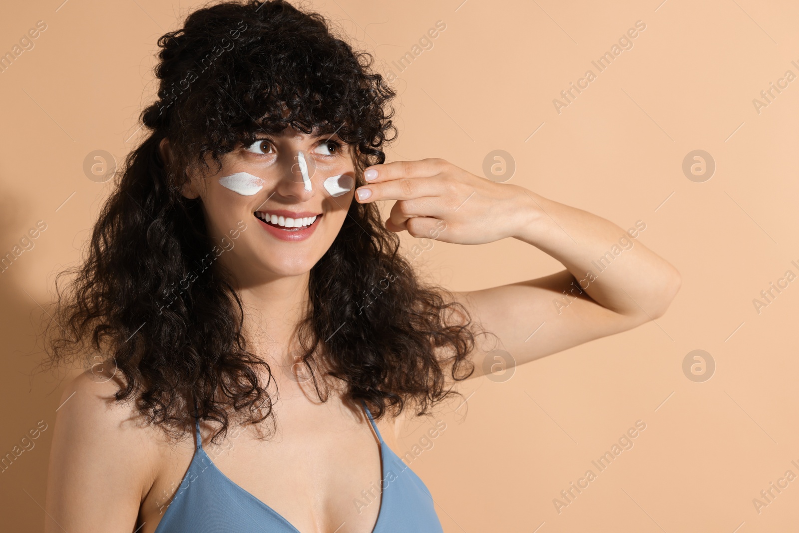 Photo of Beautiful young woman applying sun protection cream onto face on beige background