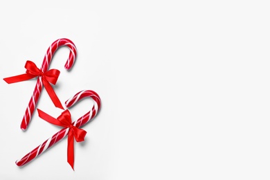 Photo of Sweet Christmas candy canes with red bows on white  background, top view. Space for text