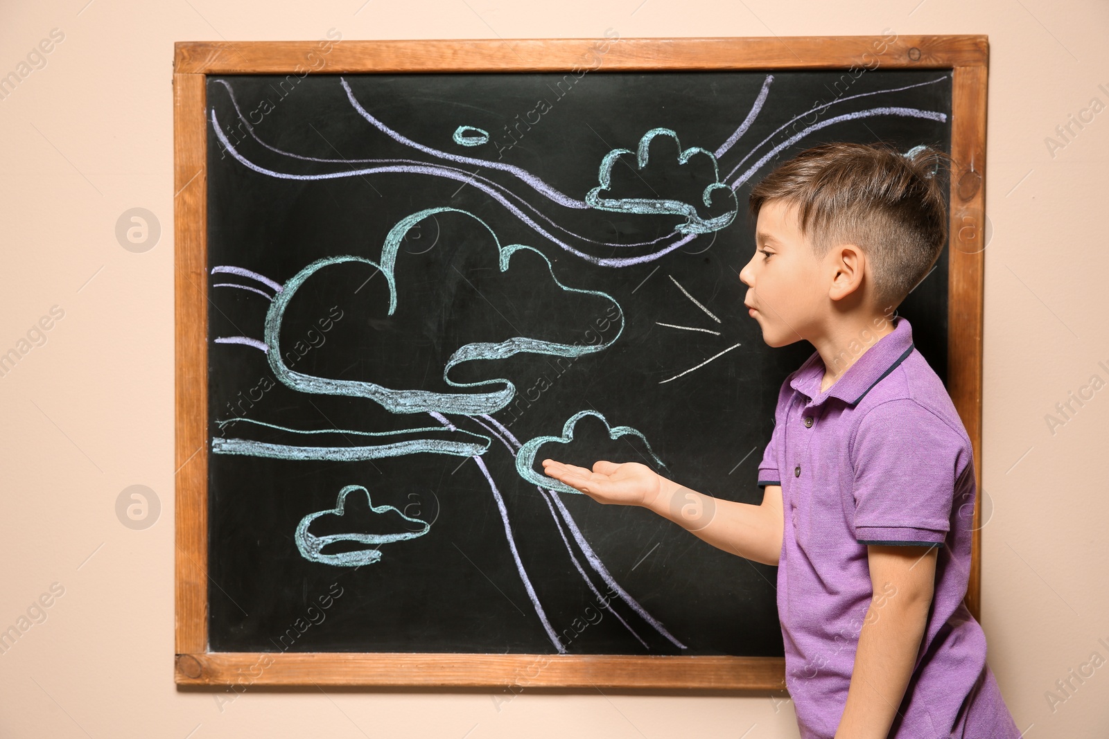 Photo of Cute little child playing at blackboard with chalk drawn sky and clouds