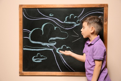 Photo of Cute little child playing at blackboard with chalk drawn sky and clouds