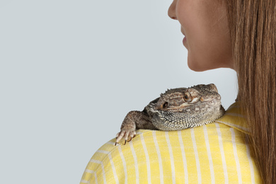 Woman with bearded lizard on grey background, closeup. Exotic pet