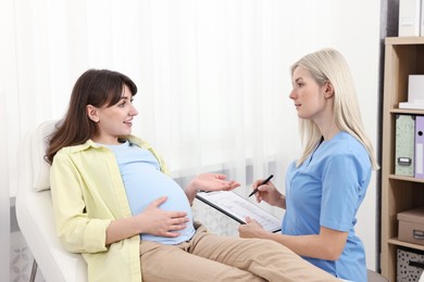 Doctor with clipboard consulting pregnant patient in clinic