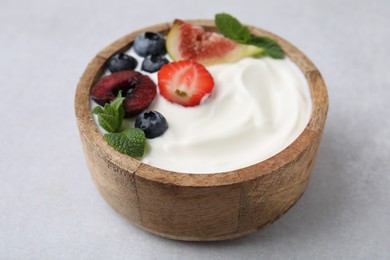 Photo of Bowl with yogurt, berries, fruits and mint on light grey table, closeup