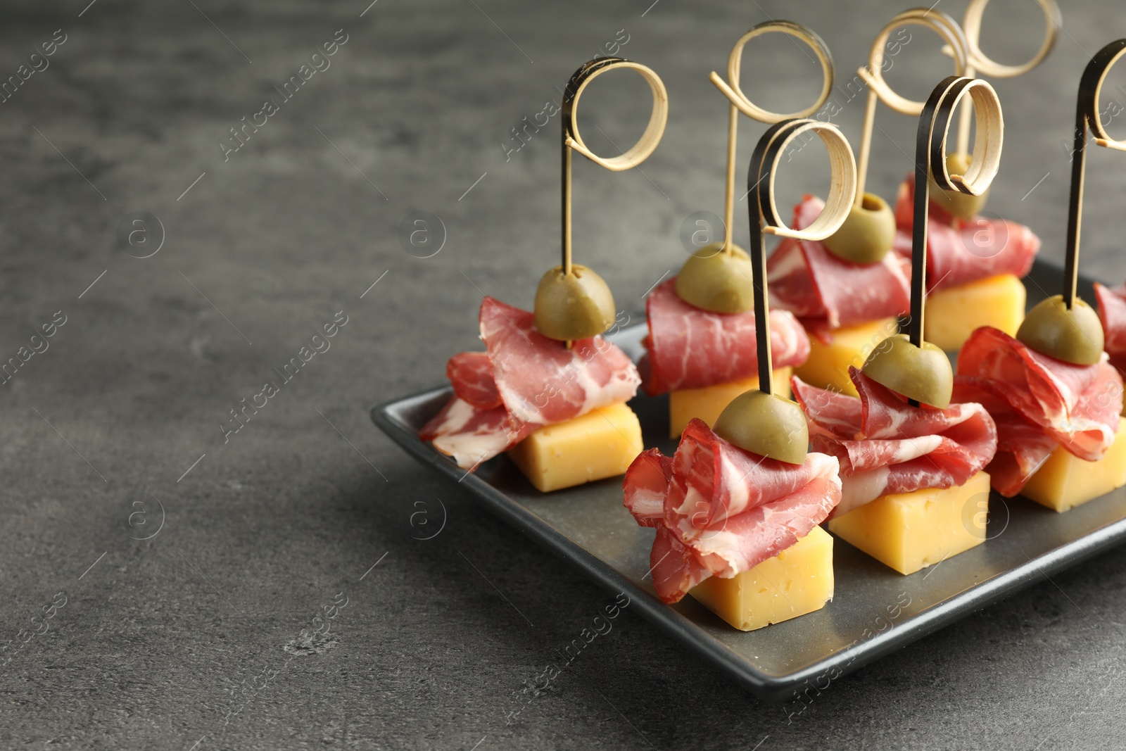 Photo of Tasty canapes with olives, prosciutto and cheese on grey table, closeup. Space for text