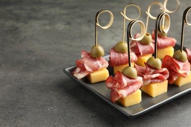 Tasty canapes with olives, prosciutto and cheese on grey table, closeup. Space for text