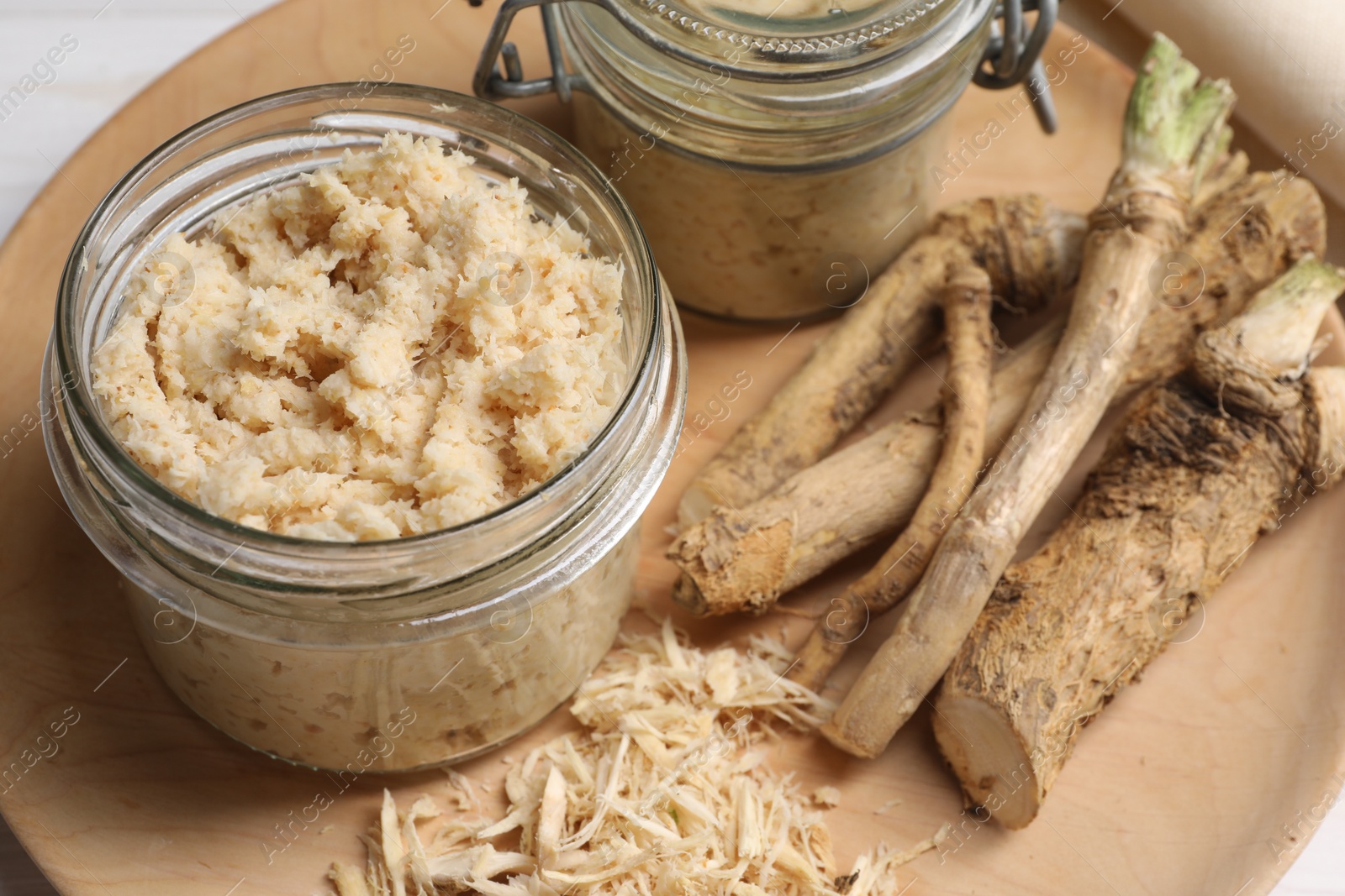 Photo of Tasty prepared horseradish and roots on wooden platter, closeup