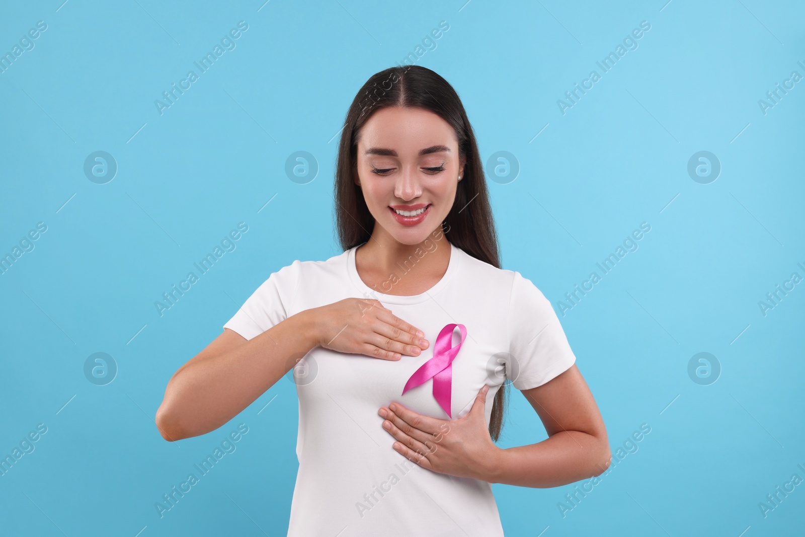 Photo of Beautiful happy woman with pink ribbon on light blue background. Breast cancer awareness