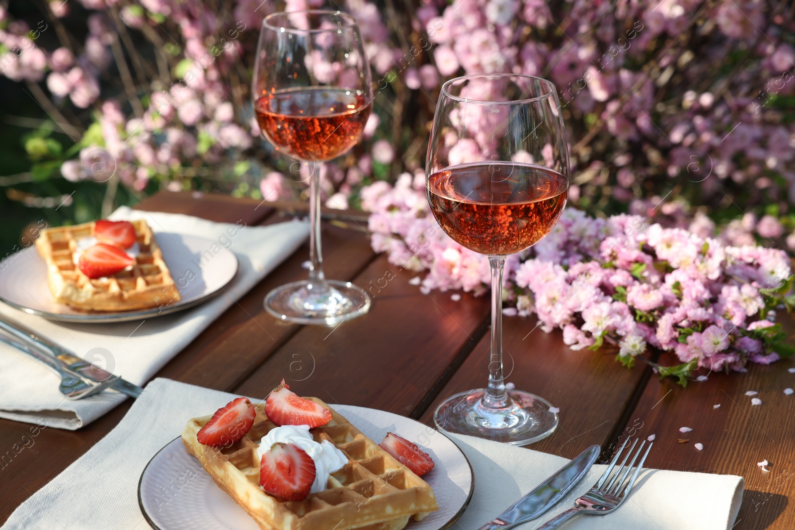 Photo of Delicious Belgian waffles with fresh strawberries and wine served on table in spring garden