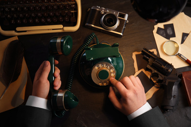 Photo of Detective dialing number on vintage telephone at table, top view