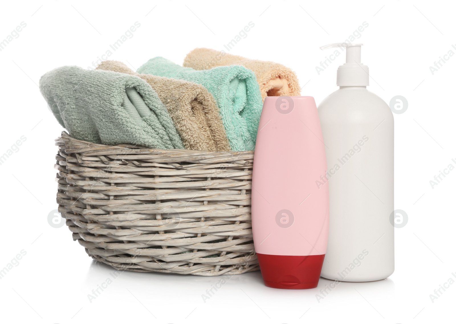 Photo of Soft towels in wicker basket and bottles of cosmetic products on white background