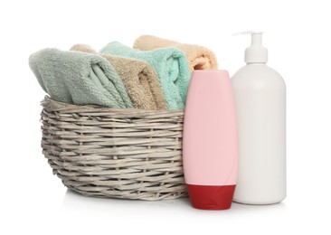 Photo of Soft towels in wicker basket and bottles of cosmetic products on white background