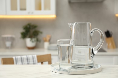 Jug and glass with clear water on white table in kitchen, space for text