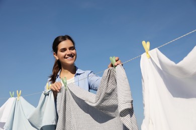 Photo of Smiling woman hanging clothes with clothespins on washing line for drying against blue sky