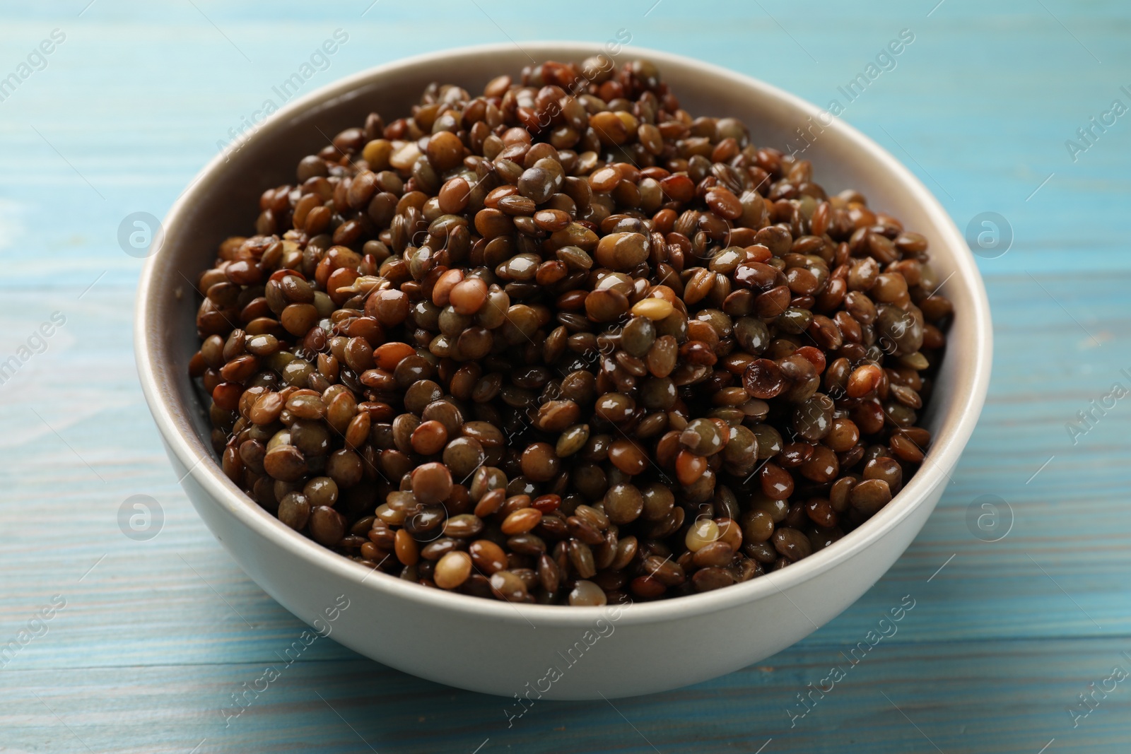 Photo of Delicious lentils in bowl on light blue wooden table, closeup