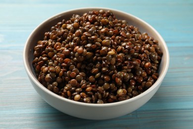 Delicious lentils in bowl on light blue wooden table, closeup