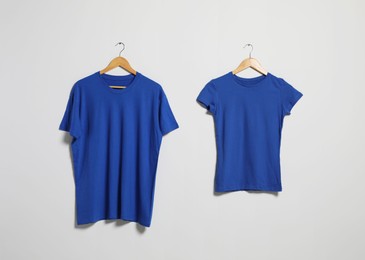 Photo of Hangers with different t-shirts on light wall. Mockup for design