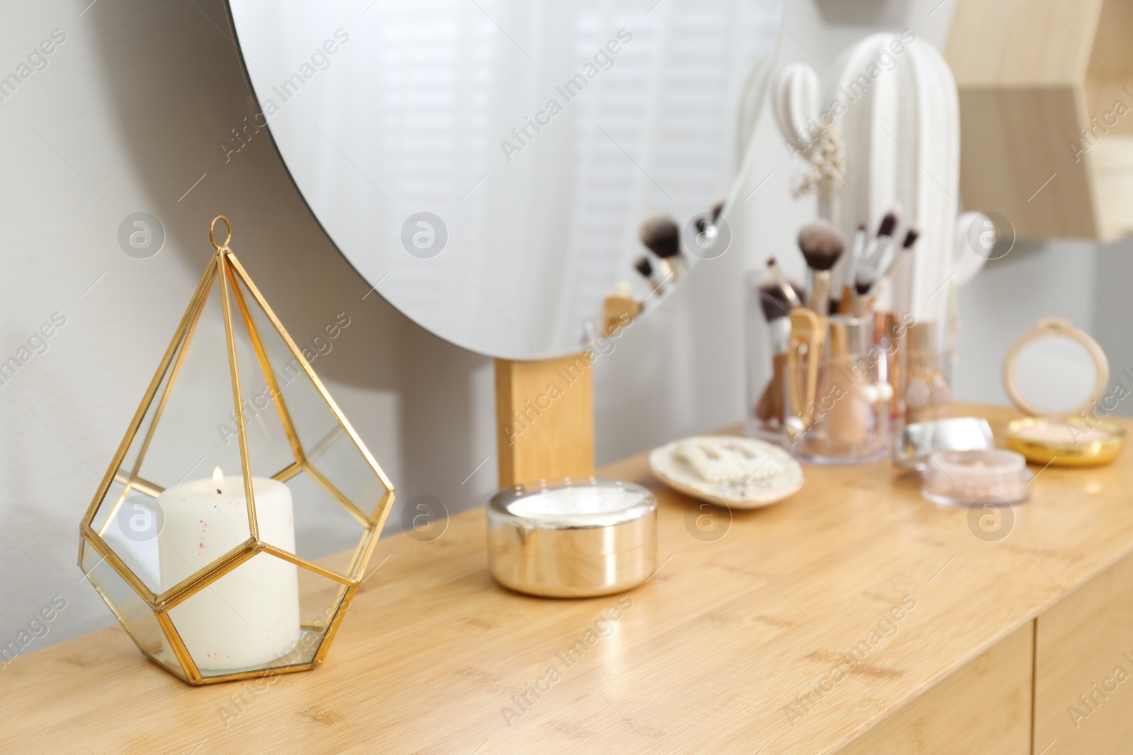 Photo of Burning white candle in holder on wooden dressing table near light wall