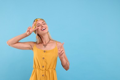 Photo of Portrait of smiling hippie woman showing peace signs on light blue background. Space for text