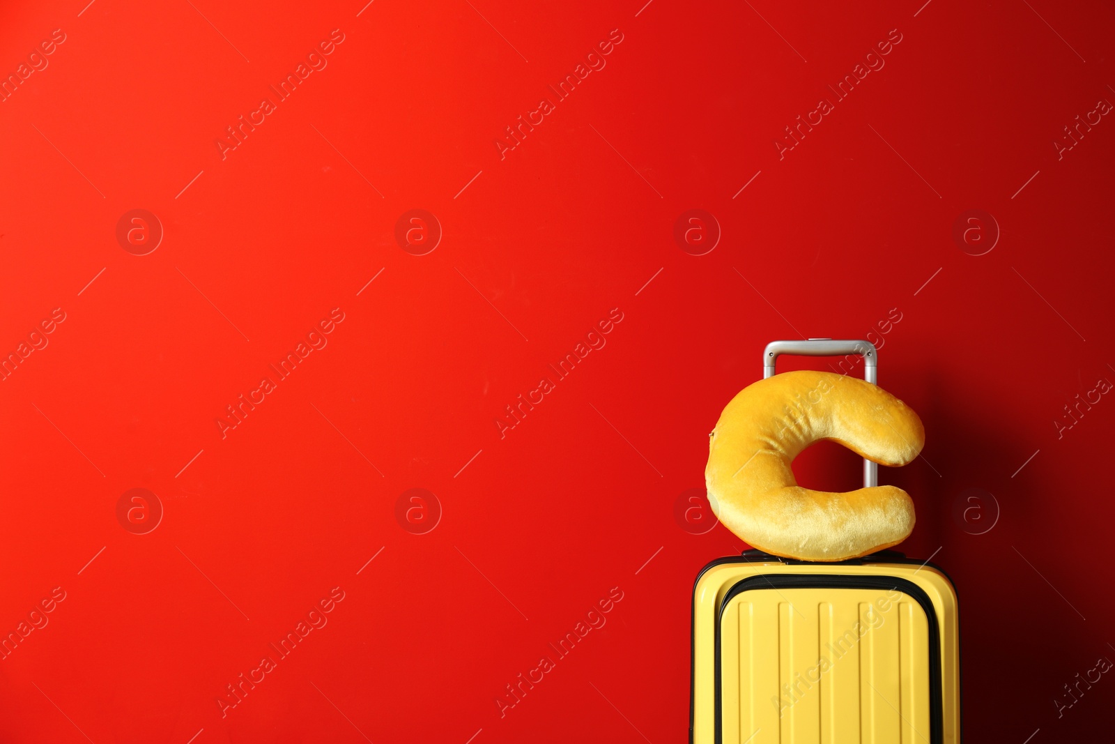 Photo of Yellow suitcase and travel pillow on red background, space for text