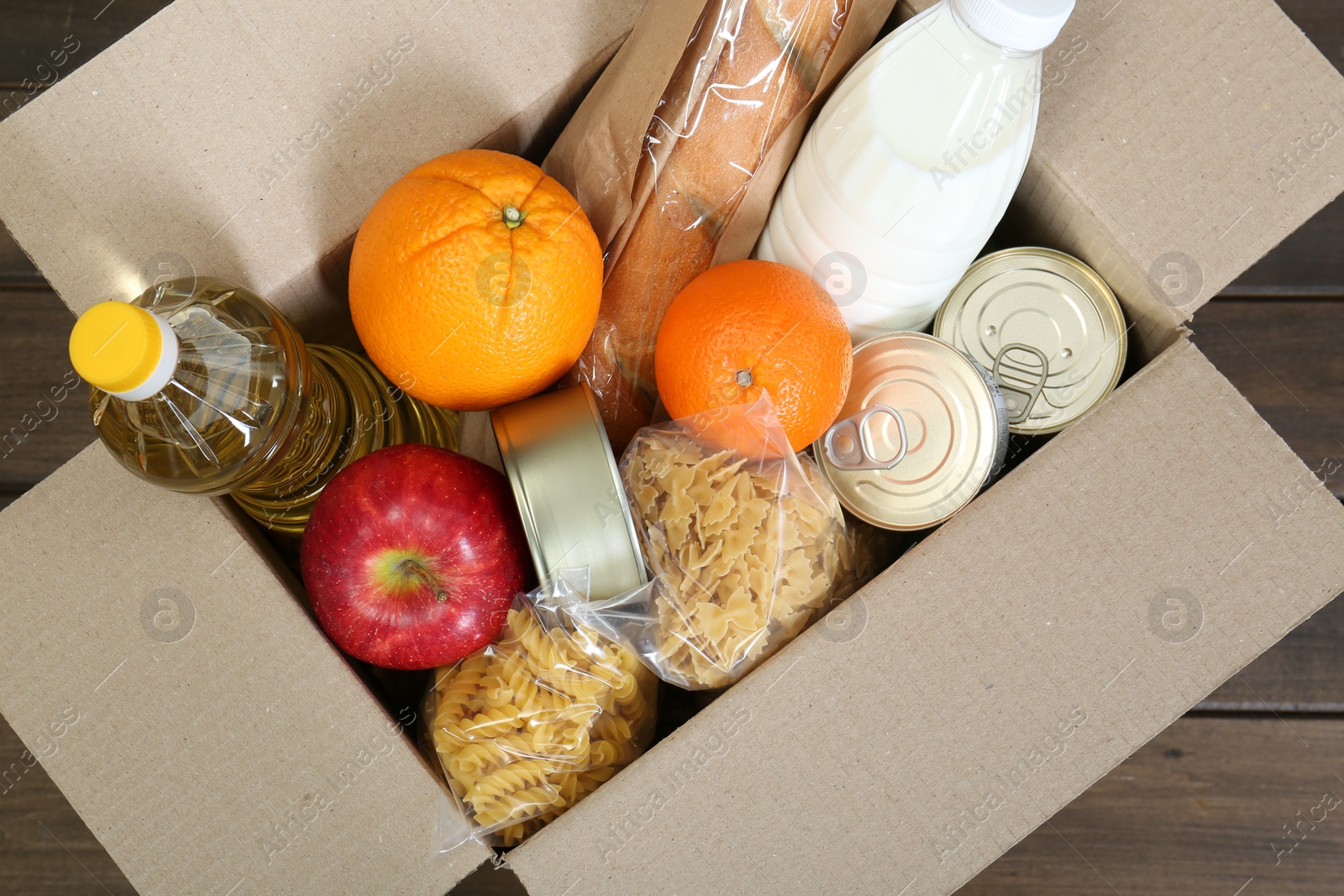 Photo of Cardboard box with donation food on wooden table, top view