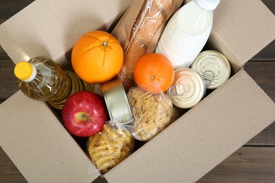 Cardboard box with donation food on wooden table, top view