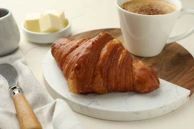 Tasty croissant served with cup of hot drink on light table, closeup