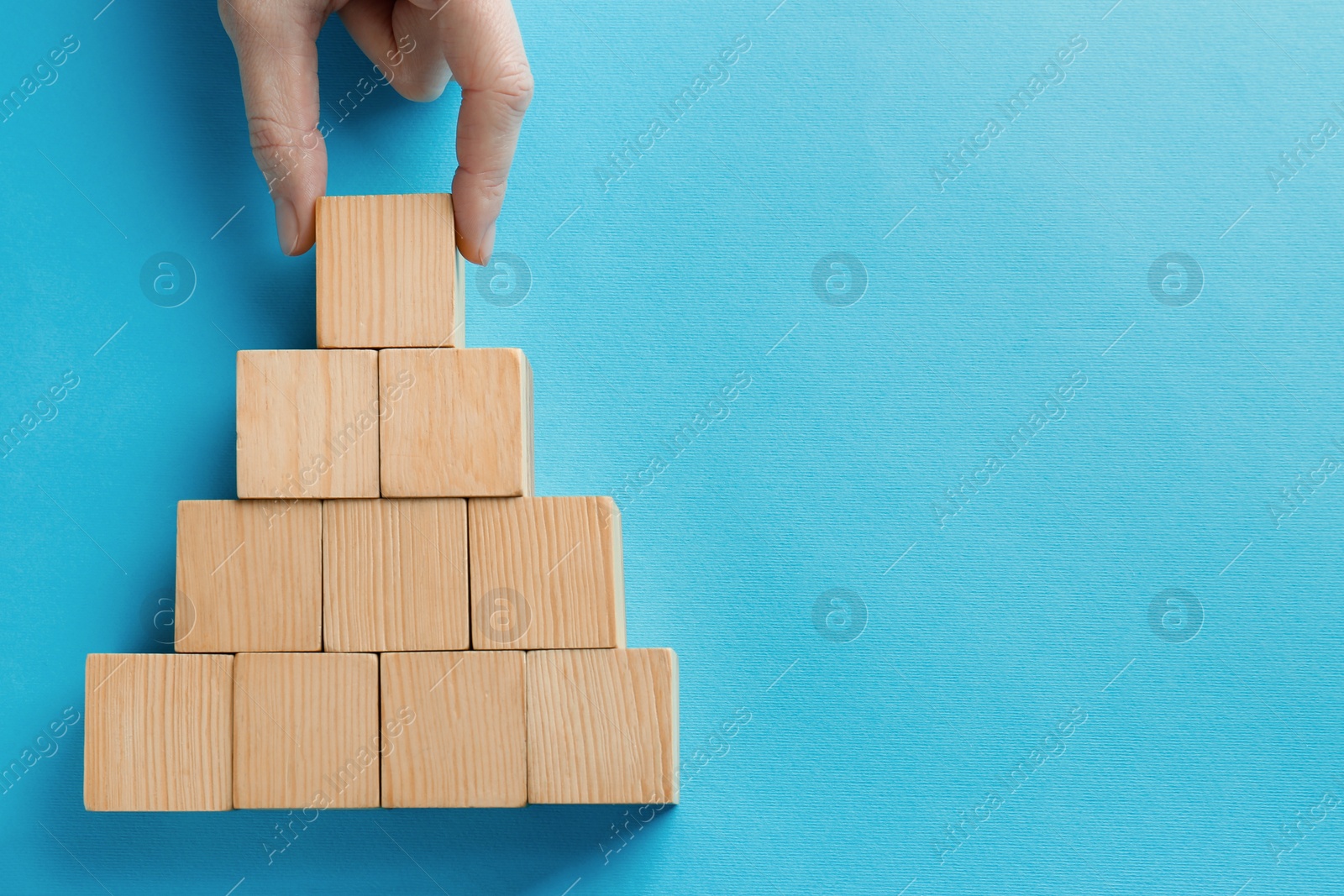 Photo of Woman arranging blank wooden cubes on light blue background, top view. Space for text