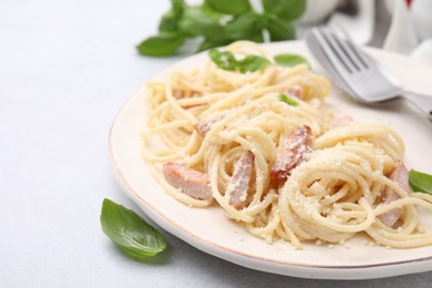 Photo of Plate of tasty pasta Carbonara with basil leaves on light grey table, closeup. Space for text