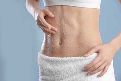 Young woman applying natural scrub on her belly against color background, closeup