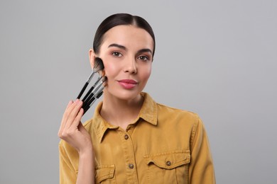 Beautiful woman with different makeup brushes on light grey background