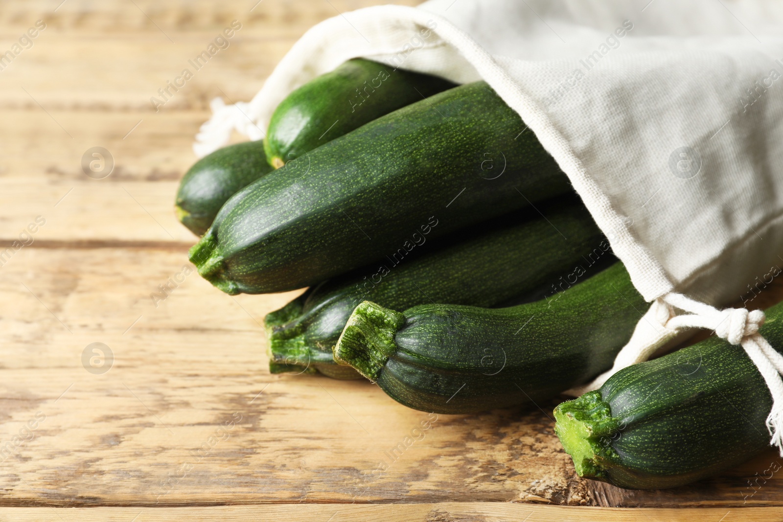 Photo of Sack with green ripe zucchinis on wooden table, closeup