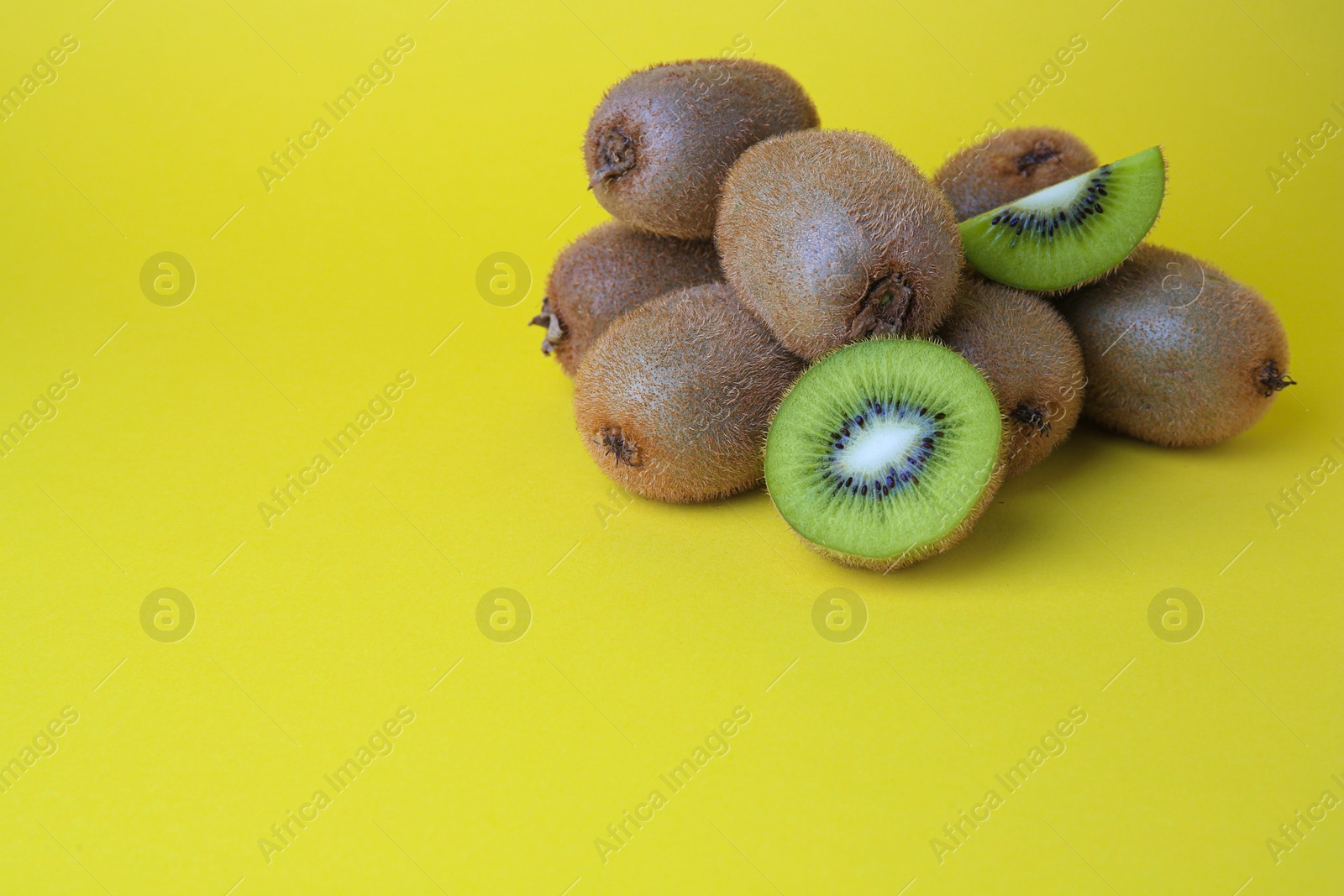 Photo of Heap of whole and cut fresh kiwis on yellow background, space for text