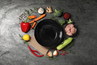 Empty iron wok surrounded by ingredients on grey table, flat lay