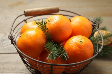 Photo of Fresh tangerines with fir tree branches in metal basket on wooden table, closeup. Christmas atmosphere