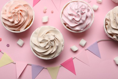 Photo of Delicious birthday cupcakes, bunting flags, marshmallows and sprinkles on pink background, flat lay