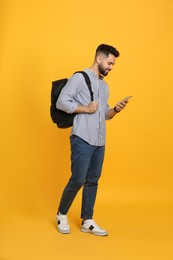 Young man with stylish backpack and smartphone on yellow background