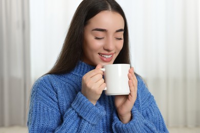 Photo of Happy young woman holding white ceramic mug at home