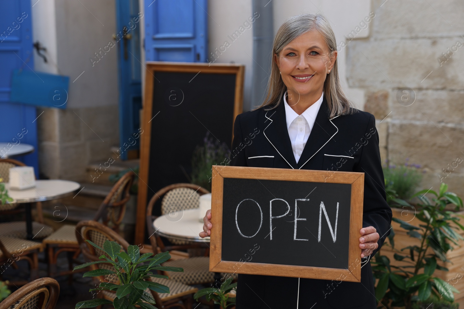 Photo of Happy business owner holding open sign near her cafe outdoors, space for text