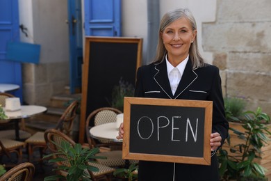 Photo of Happy business owner holding open sign near her cafe outdoors, space for text
